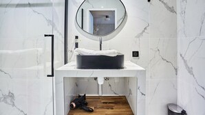 A bathroom with a white marble sink, a round mirror, and a towel rack.