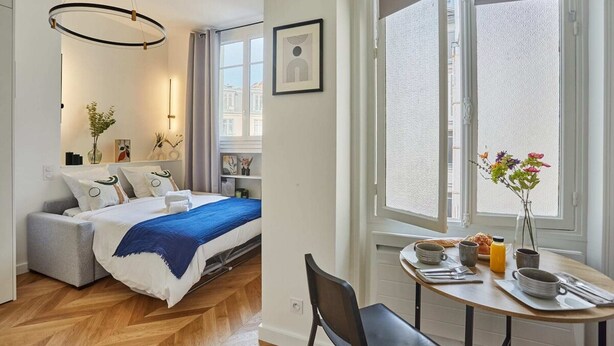 Een moderne slaapkamer met een bed, nachtkastje en een uitzicht op de stad door grote ramen.