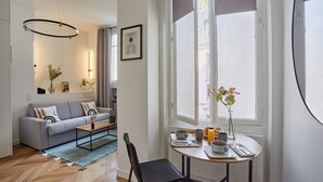 Een moderne woonkamer met een grijze bank, een salontafel en een eethoek met een tafel gedekt voor twee personen.