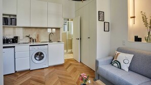 Een compacte keuken met een wasmachine, een grijze bank en een visgraatvloer.