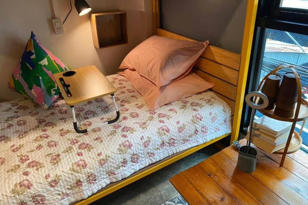 Een knus slaapkamer met een bed, een klein bureau, een lamp en een raam met uitzicht.