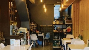 L’intérieur d’un restaurant se caractérise par de hauts plafonds, des poutres apparentes en bois et des luminaires suspendus. Les tables et les chaises sont disposées pour accueillir les clients.