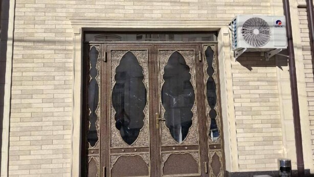 A building with a sign reading "Oks Hotel" above a large, ornate wooden door. There are two air conditioning units mounted on the wall above the door. - OKS hotel (Tashkent)