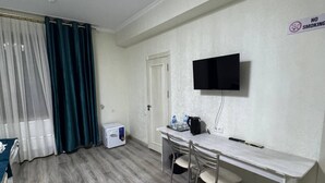 A room with a wooden floor, a desk with chairs, a television mounted on the wall, and a 'No Smoking' sign. - OKS hotel (Tashkent)