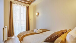 Una habitación de hotel con cama, cortinas, una lámpara fijada a la pared y un radiador.