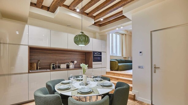 Una cocina moderna con armarios blancos, una pared de acento de madera y un comedor con una mesa redonda para cuatro.