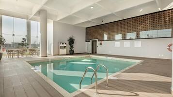 Una piscina interior moderna con agua cristalina, un muelle de madera y vistas a la ciudad.