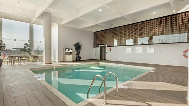A modern indoor swimming pool with clear water, a wooden deck, and a view of the city. - Holiday Inn & Suites Aguascalientes (Aguascalientes)