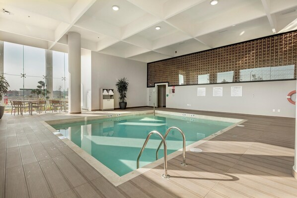 A modern indoor swimming pool with clear water, a wooden deck, and a view of the city. - Holiday Inn & Suites Aguascalientes (Aguascalientes)