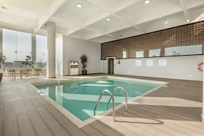 A modern indoor swimming pool with clear water, a wooden deck, and a view of the city. - Holiday Inn & Suites Aguascalientes (Aguascalientes)