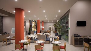 A modern restaurant with round tables and chairs, a TV, and a glass wall. - Holiday Inn & Suites Aguascalientes (Aguascalientes)