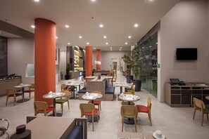 A modern restaurant with round tables and chairs, a TV, and a glass wall. - Holiday Inn & Suites Aguascalientes (Aguascalientes)