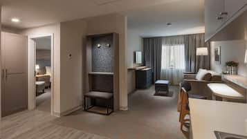A modern hotel room with a kitchenette, a seating area with a sofa and chairs, a small table, and a TV.