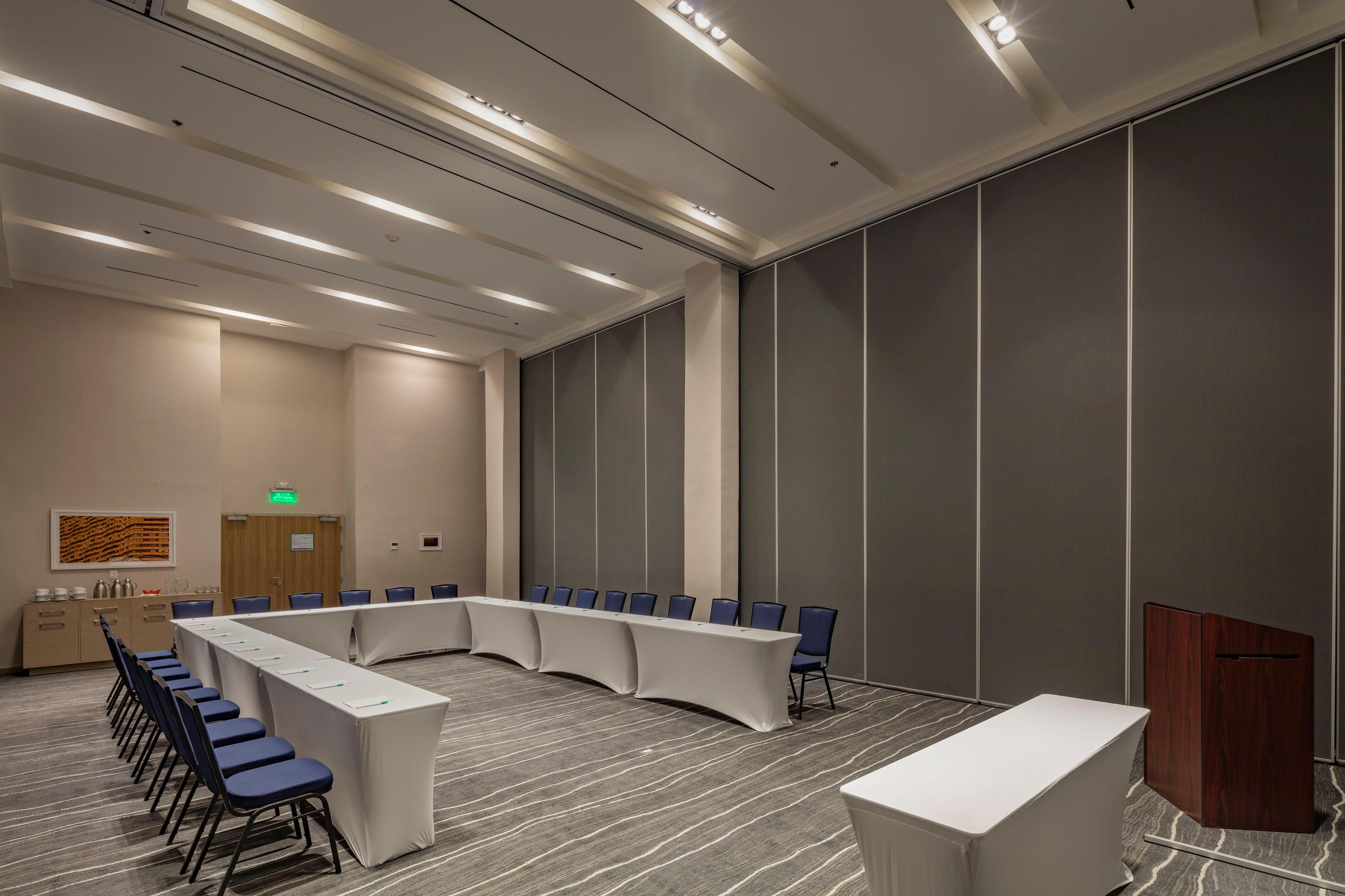 Uma sala de conferências com uma mesa comprida, cadeiras, um púlpito e um armário de madeira.