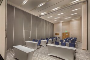 A conference room with rows of chairs and tables, a door, and a wall with a panel design. - Holiday Inn & Suites Aguascalientes (Aguascalientes)