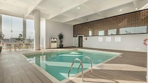 A modern indoor swimming pool with clear water, a wooden deck, and a view of the city. - Holiday Inn & Suites Aguascalientes (Aguascalientes)
