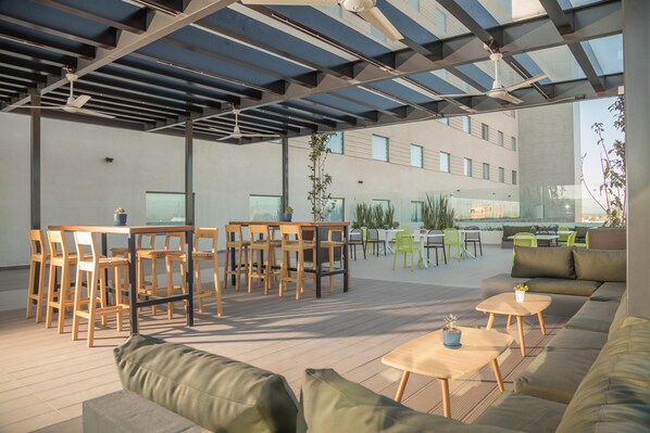 An outdoor seating area with wooden tables and chairs, a sofa, and a ceiling fan. - Holiday Inn & Suites Aguascalientes (Aguascalientes)