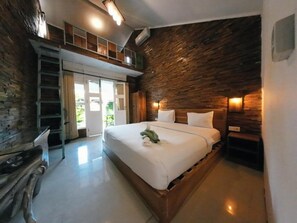 A bedroom with a wooden bed, a loft area, and a stone wall. - Habana Hotel (Kuta)