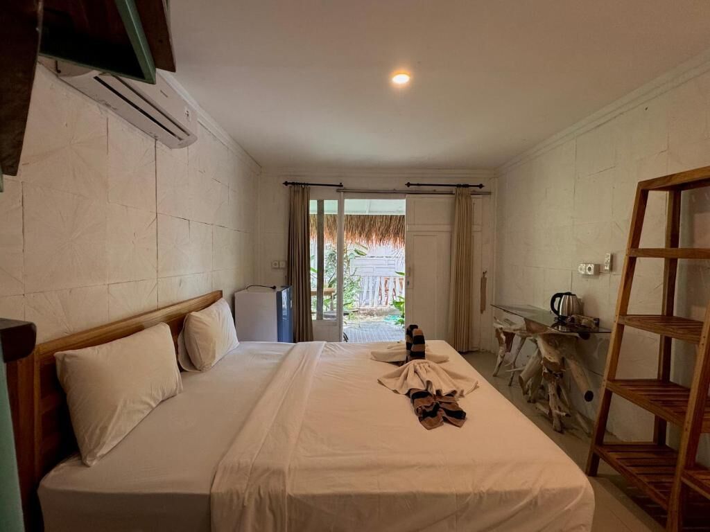 A hotel room with a bed, a wooden headboard, a small table with a kettle, and a wooden shelf.