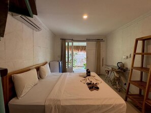 A hotel room with a bed, a wooden headboard, a small table with a kettle, and a wooden shelf. - Habana Hotel (Kuta)