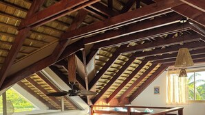 Une chambre mansardée avec un plafond en pente, des poutres en bois, un lit et un luminaire suspendu.