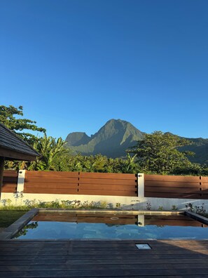 A wooden deck with a clear pool reflecting the surrounding landscape, including a mountain and lush greenery. - Perfect Moorea Getaway for Families & Friends – Pool + Beach 200m (Moorea)