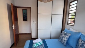 Une chambre à coucher avec un lit, un luminaire suspendu, une fenêtre avec des stores et une porte donnant sur une autre pièce.