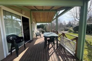 A covered outdoor area with a table and chairs, a sliding glass door, and a view of the surrounding landscape. - Charming Chalet for 6 People - Nature & Pools (Beynat)