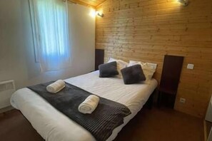 A wooden-paneled bedroom with a bed, pillows, and a blanket. - Charming Chalet for 6 People - Nature & Pools (Beynat)