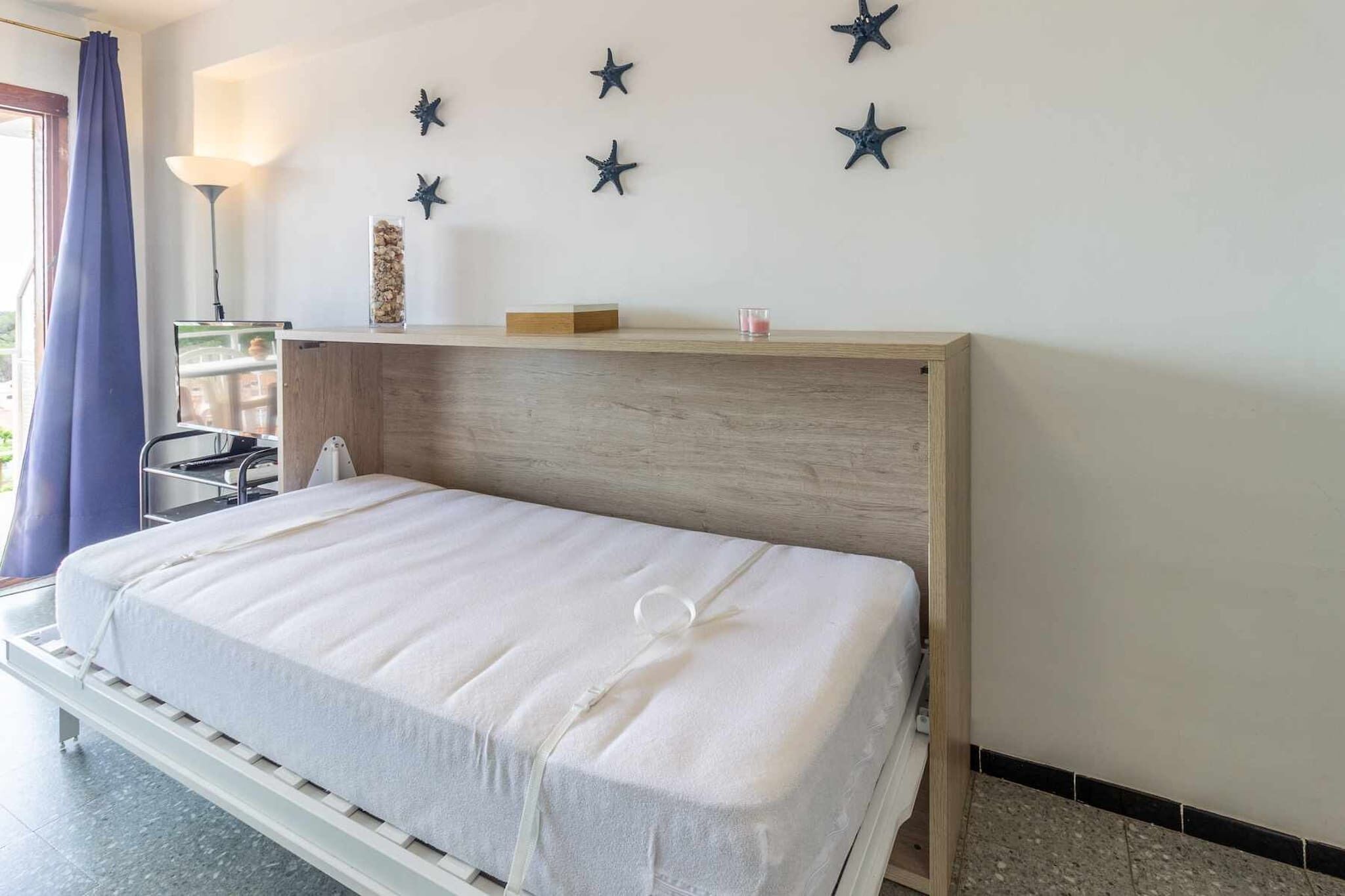 Un lit bien fait dans une chambre d’hôtel, avec une tête de lit en bois, une table de chevet avec une lampe et des décorations en forme d’étoiles sur le mur.