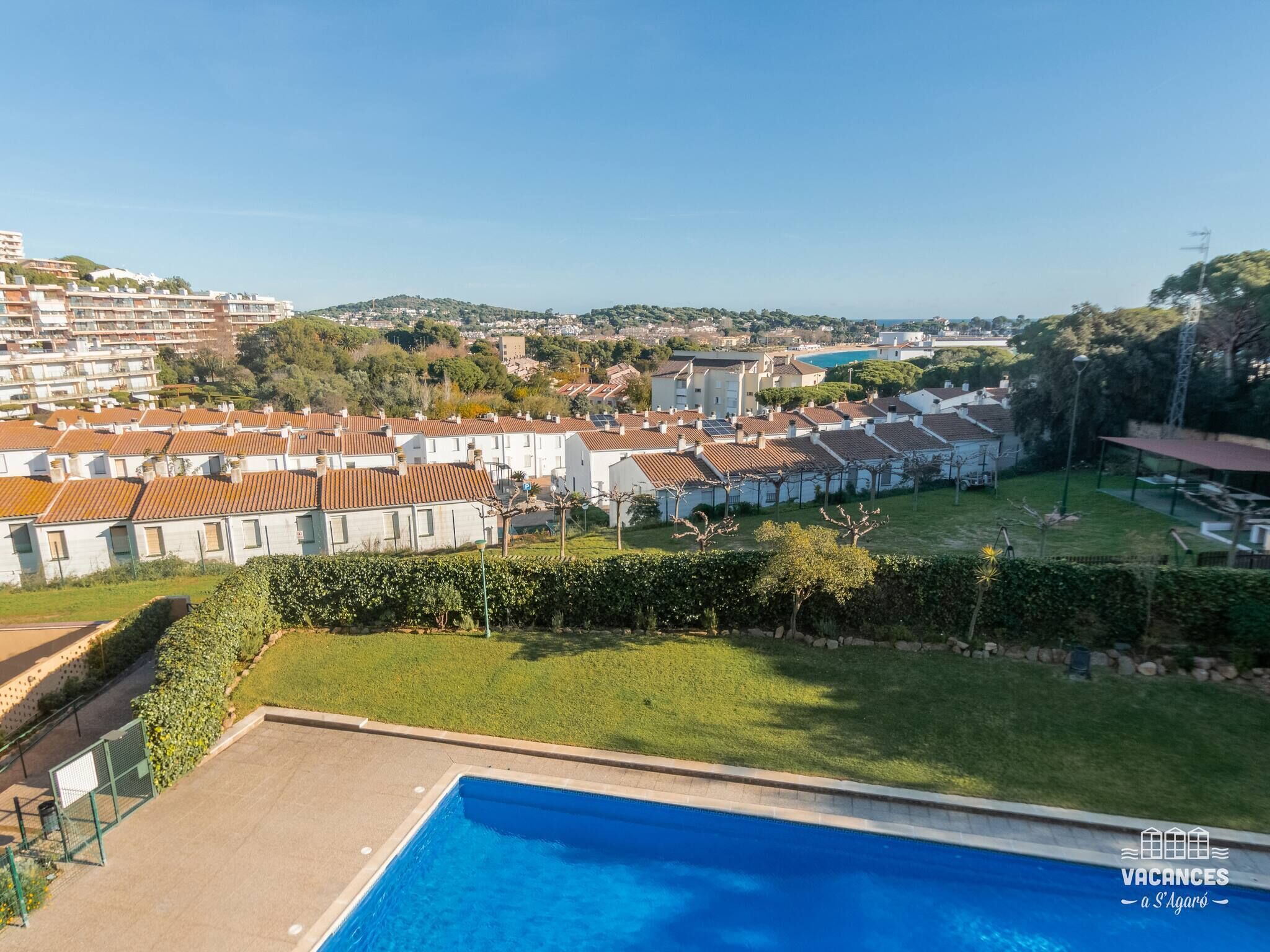 A residential area with a swimming pool, terraced houses, and a distant view of a town.