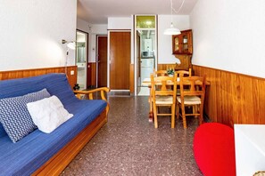 A compact living space with a blue sofa, wooden dining table, and chairs. - 27.40 Polcent 5 S'Agaró  apartment close to the beach (Sant Feliu de Guixols)