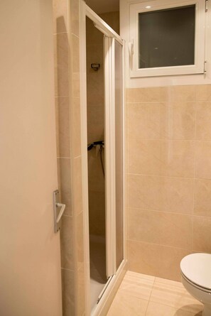 Un bagno con doccia, WC e un armadietto sopra il water.
