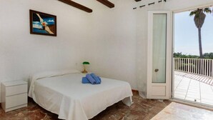 A bedroom with a bed, a nightstand, a lamp, and a view of the outside. - 08.00 Mirador House. Private pool (Platja d´Aro)