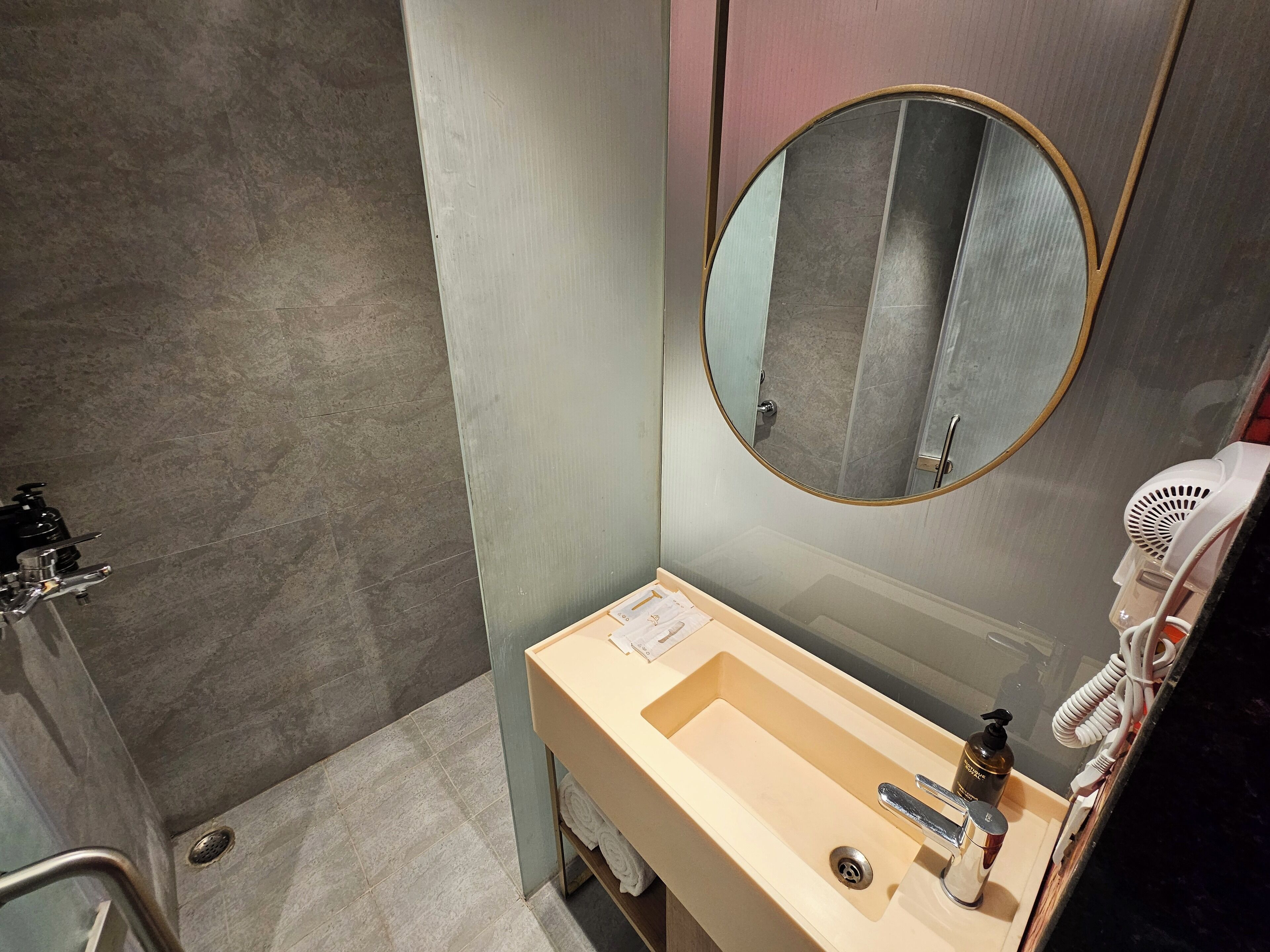 A bathroom with a beige sink, a mirror, a hairdryer, and a towel rack.