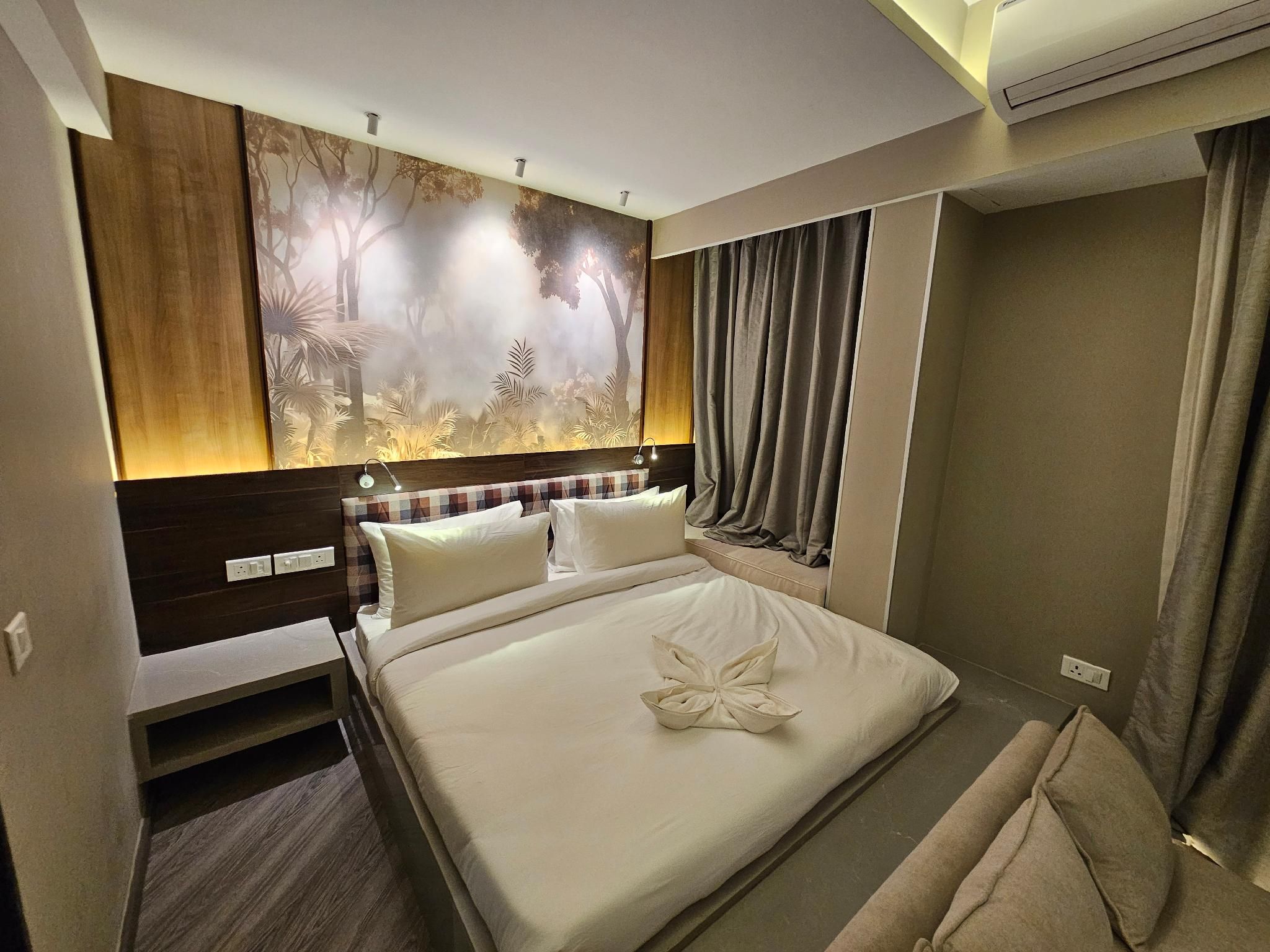 A hotel room with a large bed, a headboard with a patterned design, a wall mural, and a window with curtains.