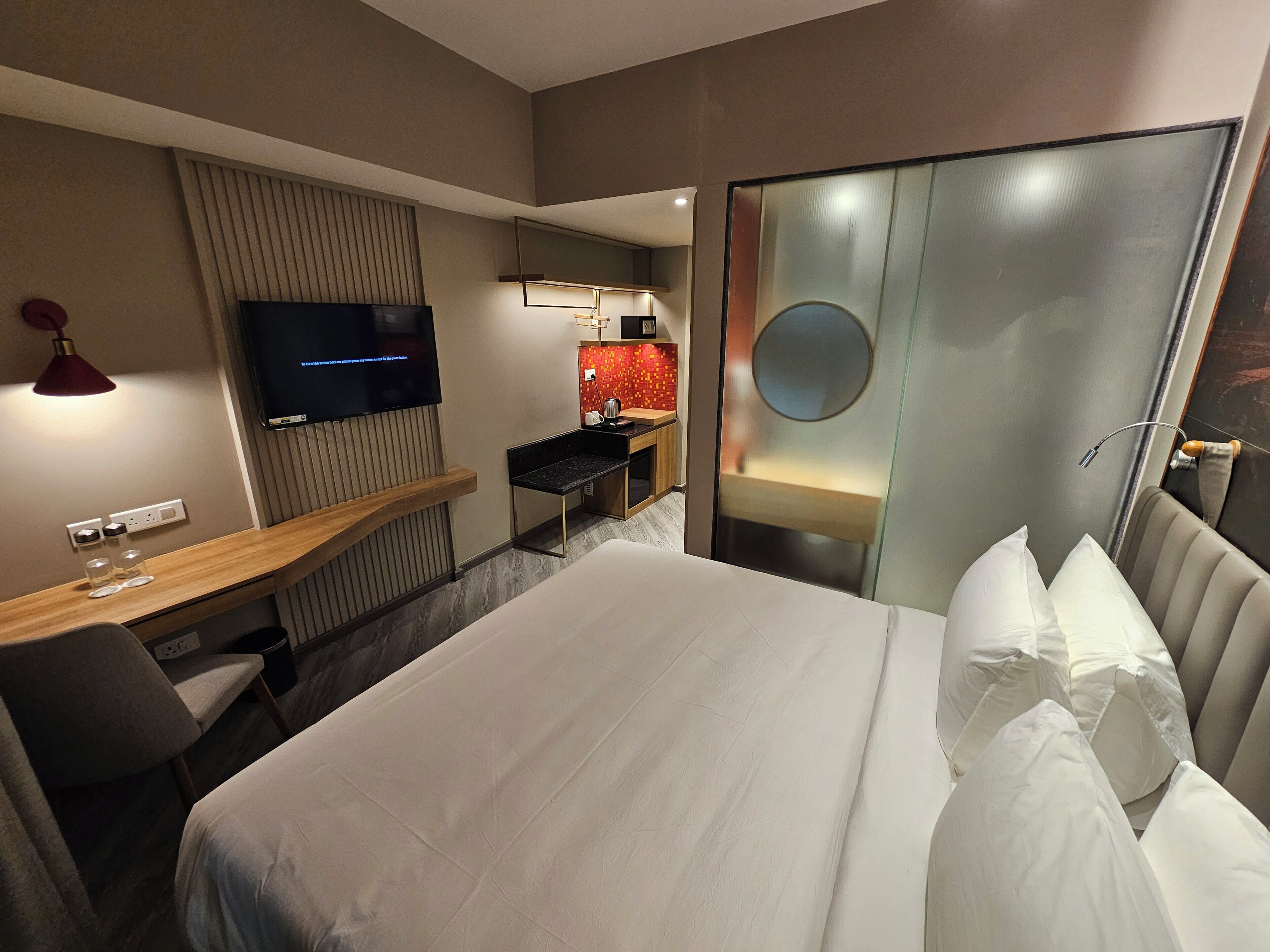 Una habitació d'hotel amb un llit gran, un escriptori, un televisor i un mini bar.