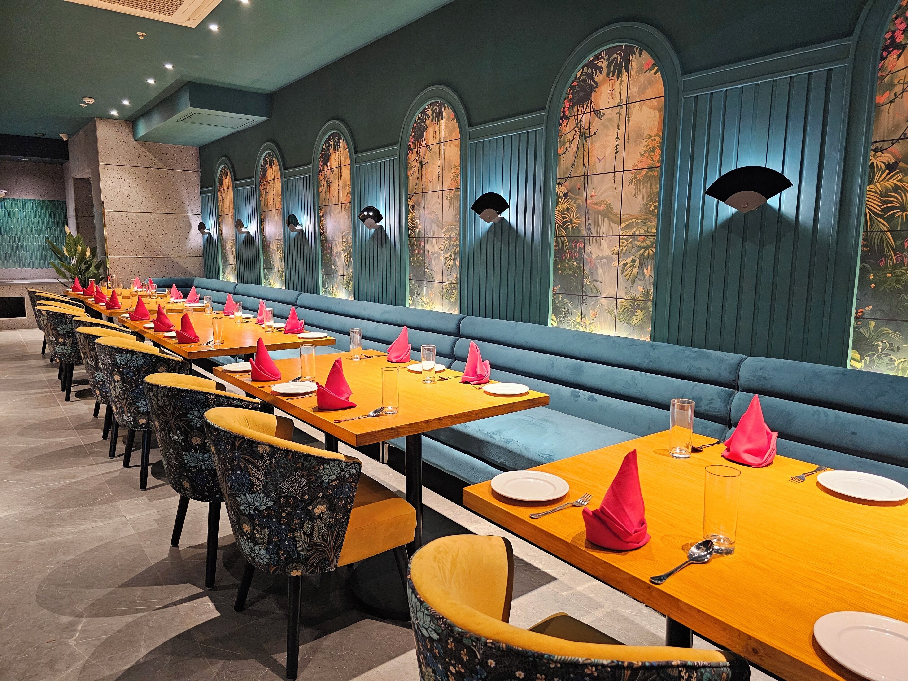 A restaurant with long tables, blue cushioned benches, and patterned chairs.