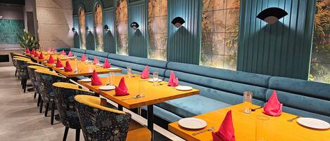 A restaurant with long tables, blue cushioned benches, and patterned chairs.