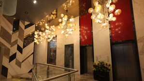 Een moderne lobby met een glazen trap, marmeren vloer en een decoratieve lamp.