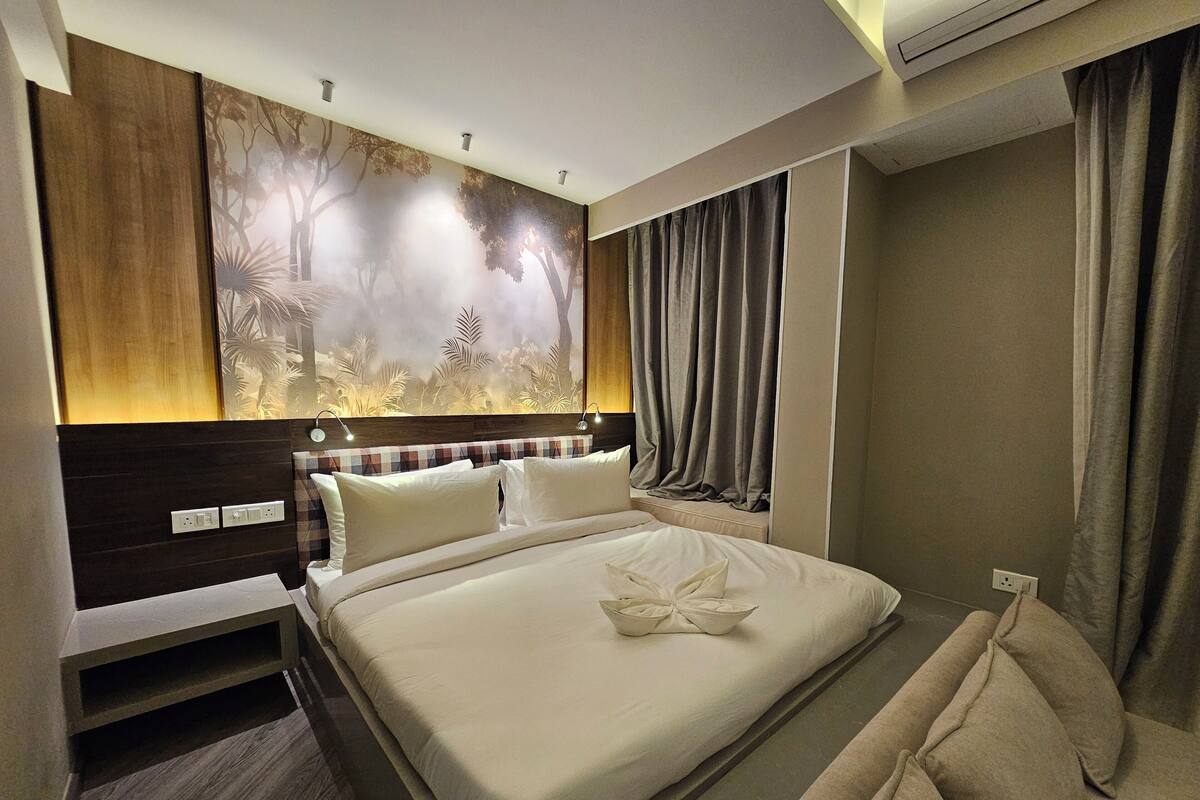 Une chambre d’hôtel avec un grand lit, une tête de lit ornée d’une fresque représentant une forêt, une table de chevet et une fenêtre avec des rideaux.