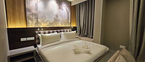Habitación de hotel con una cama grande, cabecera con un mural de un bosque, mesita de noche y ventana con cortinas.