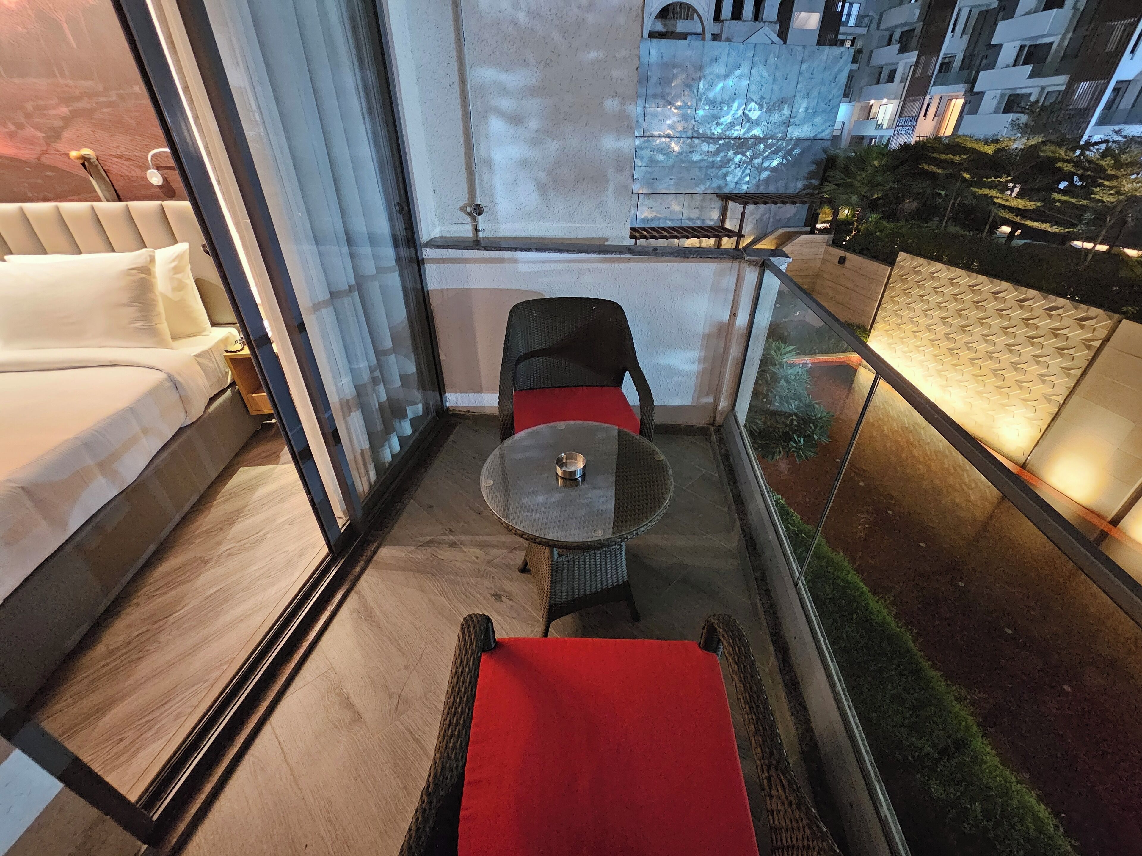 A balcony with a glass railing, a small round table, and a red cushioned bench.