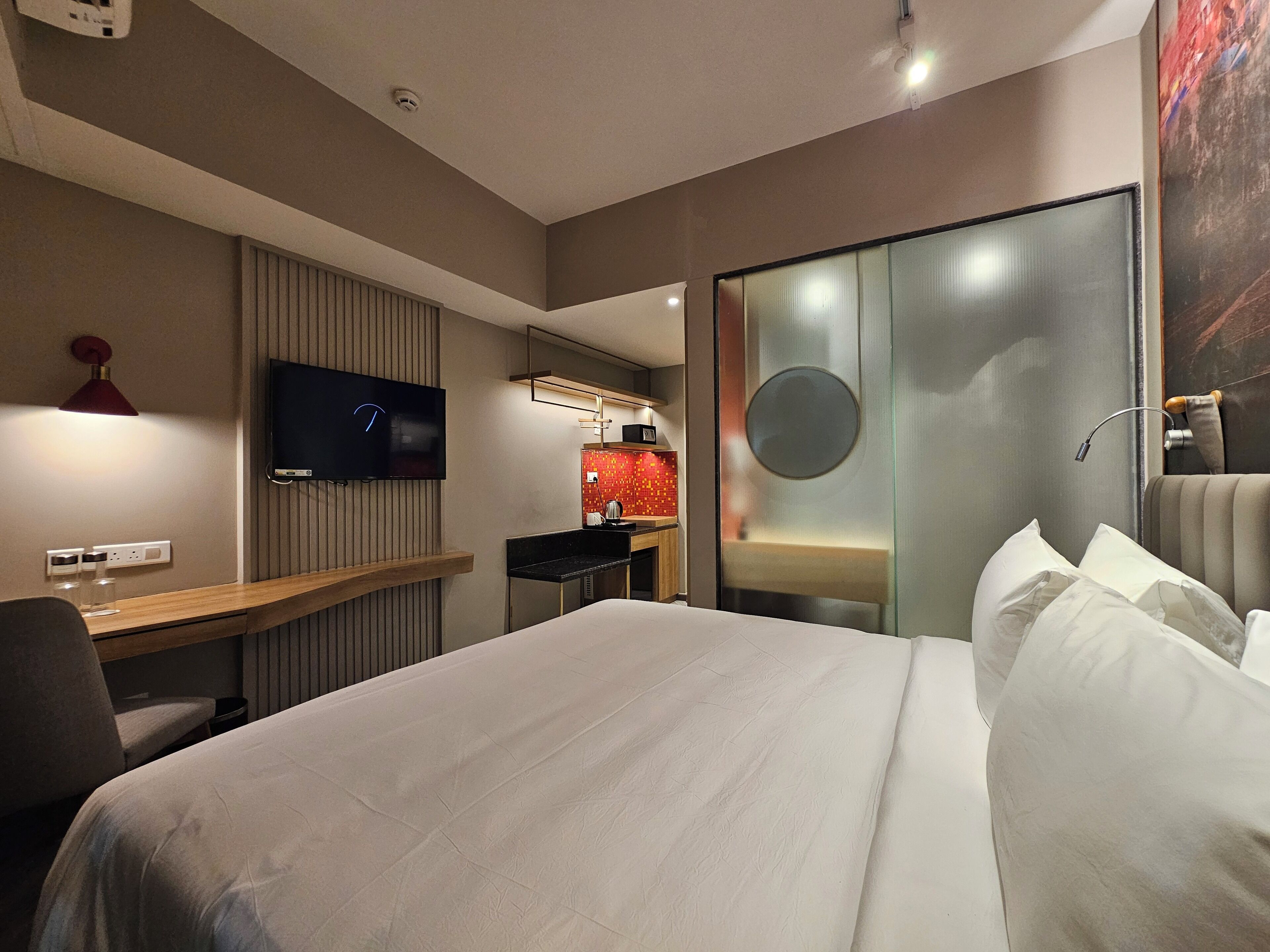 A hotel room with a bed, a desk, a television, a mirror, and a sliding door.