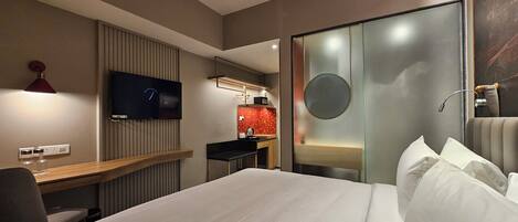 A hotel room with a bed, a desk, a television, a mirror, and a sliding door.