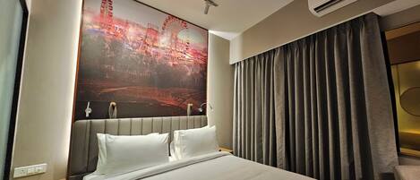 A hotel room with a large bed, a headboard with a cityscape mural, a bedside table, and a window with curtains.
