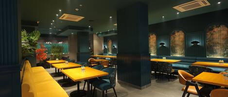 A restaurant with yellow booths, blue upholstered chairs, and tables with water bottles.