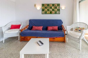 Ein gemütliches Zimmer mit einem blauen Sofa, zwei weißen Korbstühlen, einem weißen Couchtisch und einem an der Wand befestigten Gesellschaftsspiel.