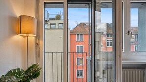 Un balcon donnant sur les bâtiments voisins, une plante en pot et une lampe fixée au mur.