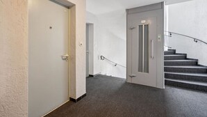 Un couloir doté d’un sol recouvert de moquette, une porte portant un numéro et un escalier muni d’une main courante.